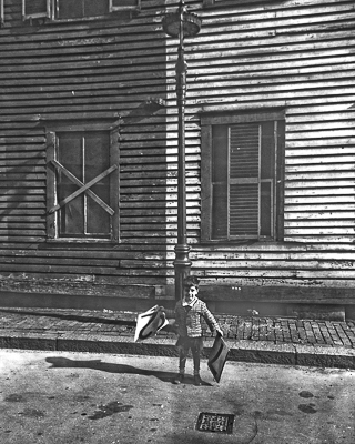 Jerry Halberstadt, 4 years old, holds number placards in front of wood frame building